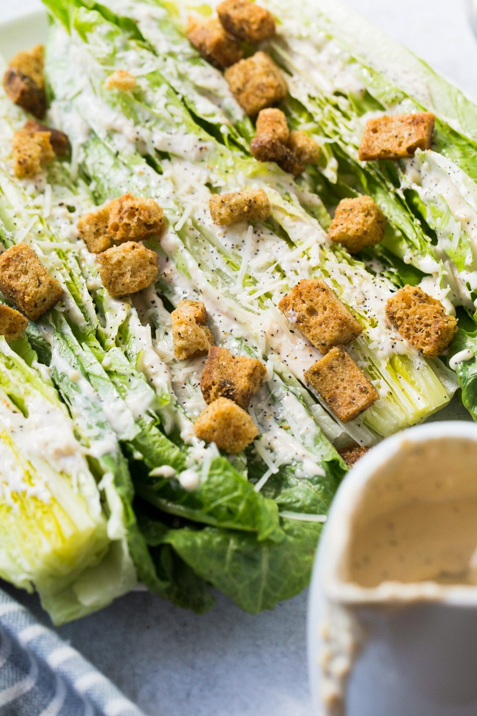 Overhead shot of hearts of romaine cut in half and smeared with caesar dressing. Some wooden spoons are placed overlapping in the bottom right.
