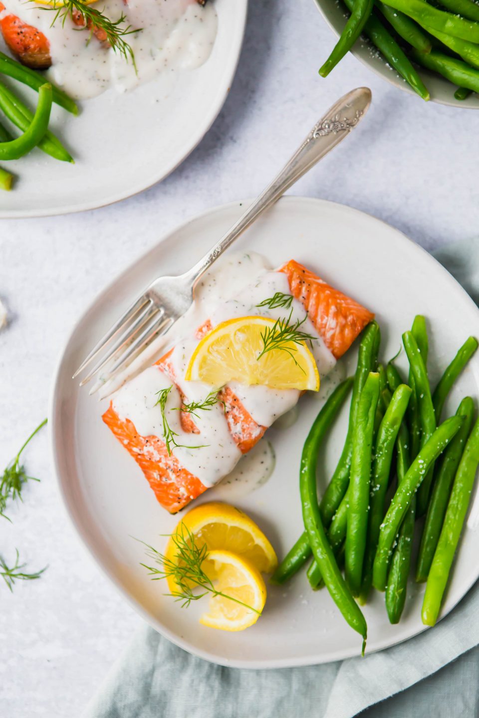 An overhead shot of a piece of salmon drizzled with a cream sauce. Lemon slices and green beans are also on the plate.